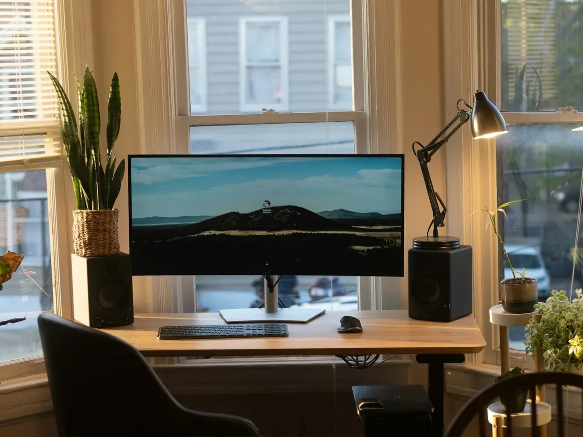 Tidy home office desk with a desktop computer and monitor by a sunny window