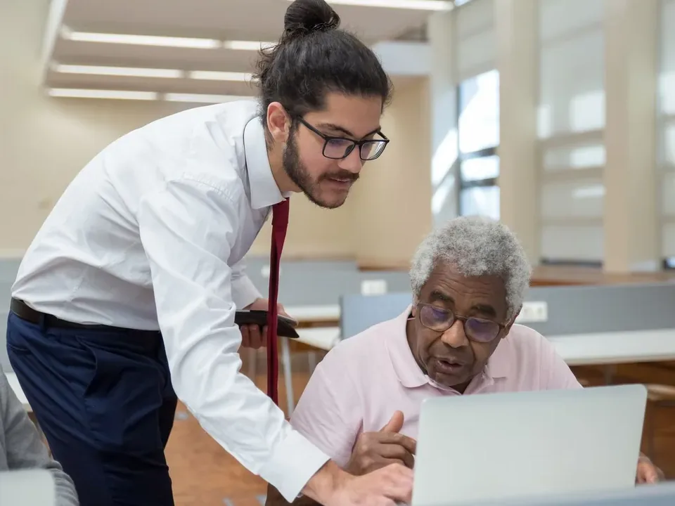 Technician leaning in to show an older man something on his laptop